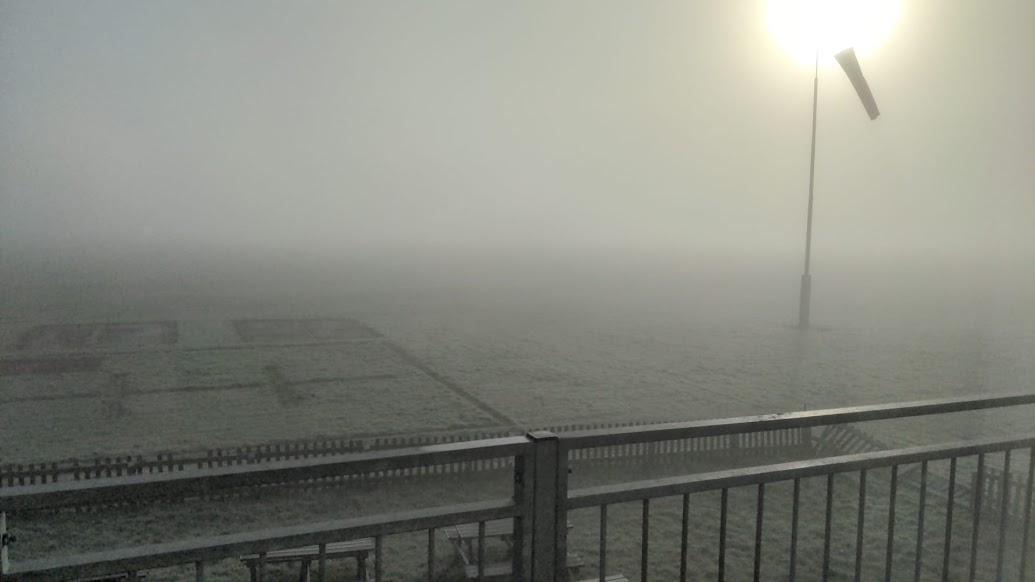 A foggy airfield, obscured sun visible behind the windsock.